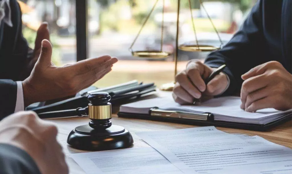 Lawyer consulting clients at a desk with documents, gavel, and scales, gesturing and taking notes.